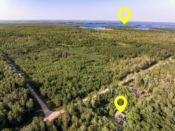 An aerial view of a forested area with a dirt road and a building with a red roof.