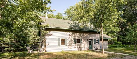 A small, single-story building with a green roof, surrounded by trees and a grassy yard.