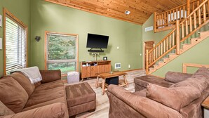 A living room with a wooden staircase, green walls, and a flat-screen TV.