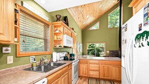 A kitchen with wooden cabinets, a white refrigerator, and a window with blinds.