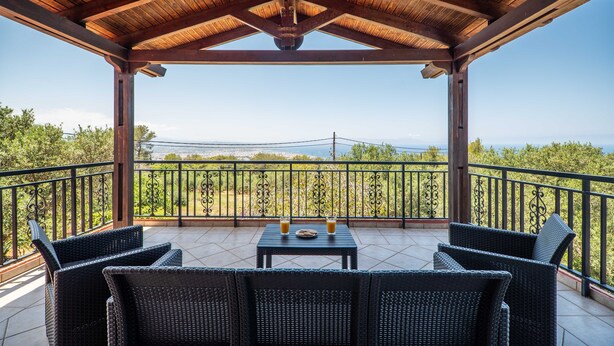 Uma área de estar coberta ao ar livre com móveis de vime, uma mesa com bebidas e vista para a paisagem.