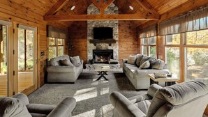 A log cabin interior with a stone fireplace, two sofas, and a television. - Log Cabin with living room fireplace and hot tub (Amberson)