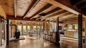 A spacious wooden cabin with a large dining area, kitchen, and a fireplace. - Log Cabin with living room fireplace and hot tub (Amberson)