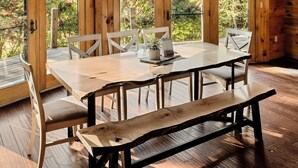 A wooden cabin interior with a large dining table, benches, and a view of the outdoors through large windows. - Log Cabin with living room fireplace and hot tub (Amberson)