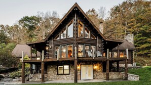 A log cabin with a stone foundation, large windows, and a balcony. - Log Cabin with living room fireplace and hot tub (Amberson)