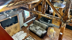Ein rustikales Blockhaus mit Kamin aus Stein, Holzbalken, einer Ledersofa und einem Fernseher.