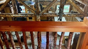 Ein rustikales Blockhaus-Interieur mit freiliegenden Holzbalken, einem erhöhten Schlafbereich und einer Küche mit Holzschränken.