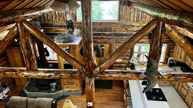 Ein rustikales Blockhaus-Interieur mit Holzbalkendecke, einem Essbereich, einer Küche und einer Sitzecke mit Sofa und Sessel.