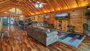 A spacious log cabin interior with a high ceiling, wooden floors, a large sofa, a dining area, and a fireplace. - Big Thunder Lodge: 180 Degree Views, 2 Kitchens (Sevierville)