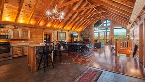 A spacious loft-style kitchen with wooden beams, a stone fireplace, and a large dining area with chairs and a table. - Big Thunder Lodge: 180 Degree Views, 2 Kitchens (Sevierville)