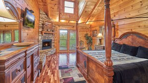 A log cabin bedroom with a four-poster bed, a stone fireplace, and a large window. - Big Thunder Lodge: 180 Degree Views, 2 Kitchens (Sevierville)