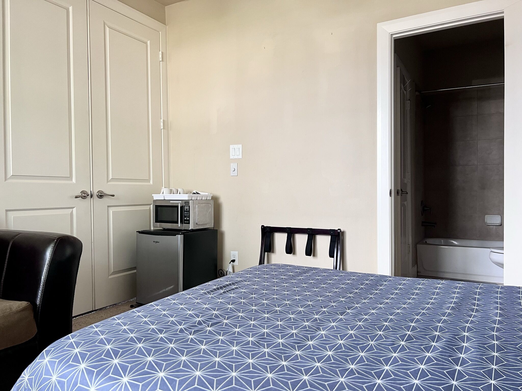 Ein Schlafzimmer mit Bett, einer Mikrowelle, einem Kühlschrank, einem Stuhl und einem Kleiderschrank.
