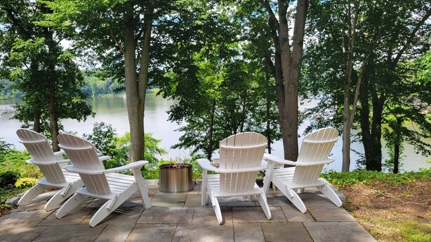 Un patio con cuatro sillas Adirondack y un brasero con vista al lago.