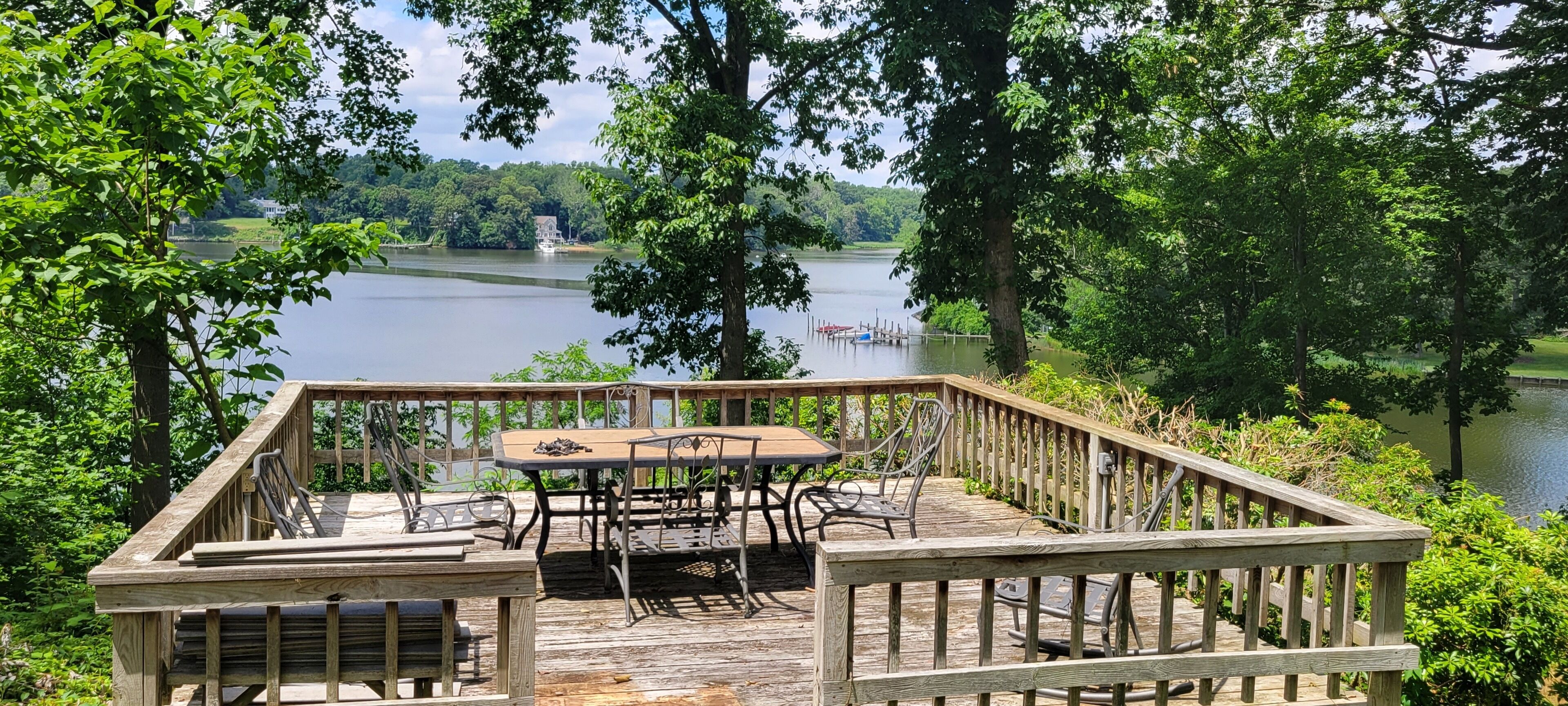 A wooden deck with a table and chairs overlooking a lake, surrounded by trees.