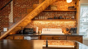 Una cocina con pared de ladrillo, escalera de madera y electrodomésticos modernos.