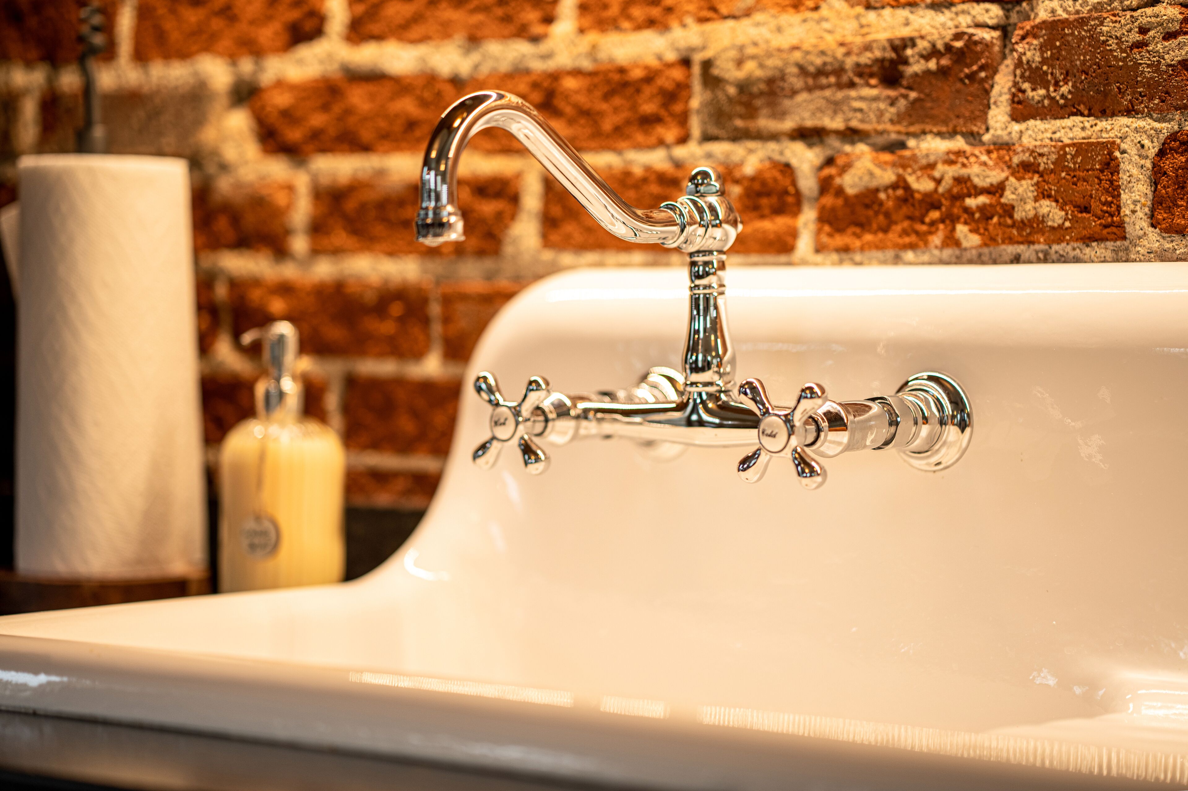 A bathroom sink with a chrome faucet, a roll of toilet paper, and a soap dispenser.