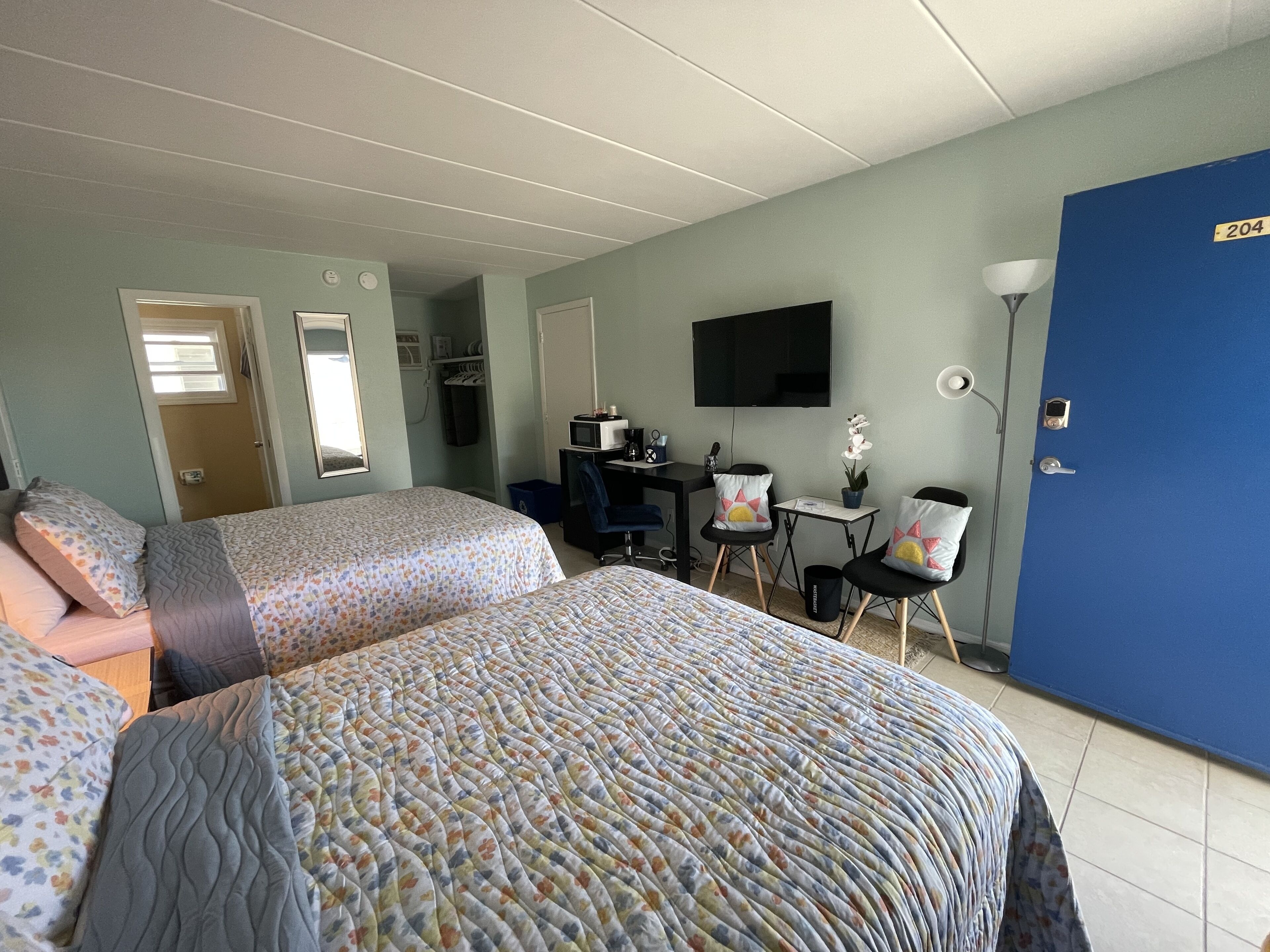 Ein Hotelzimmer mit zwei Betten, einem Schreibtisch, einem Sessel, einem Fernseher und einer Tür mit der Aufschrift 204.