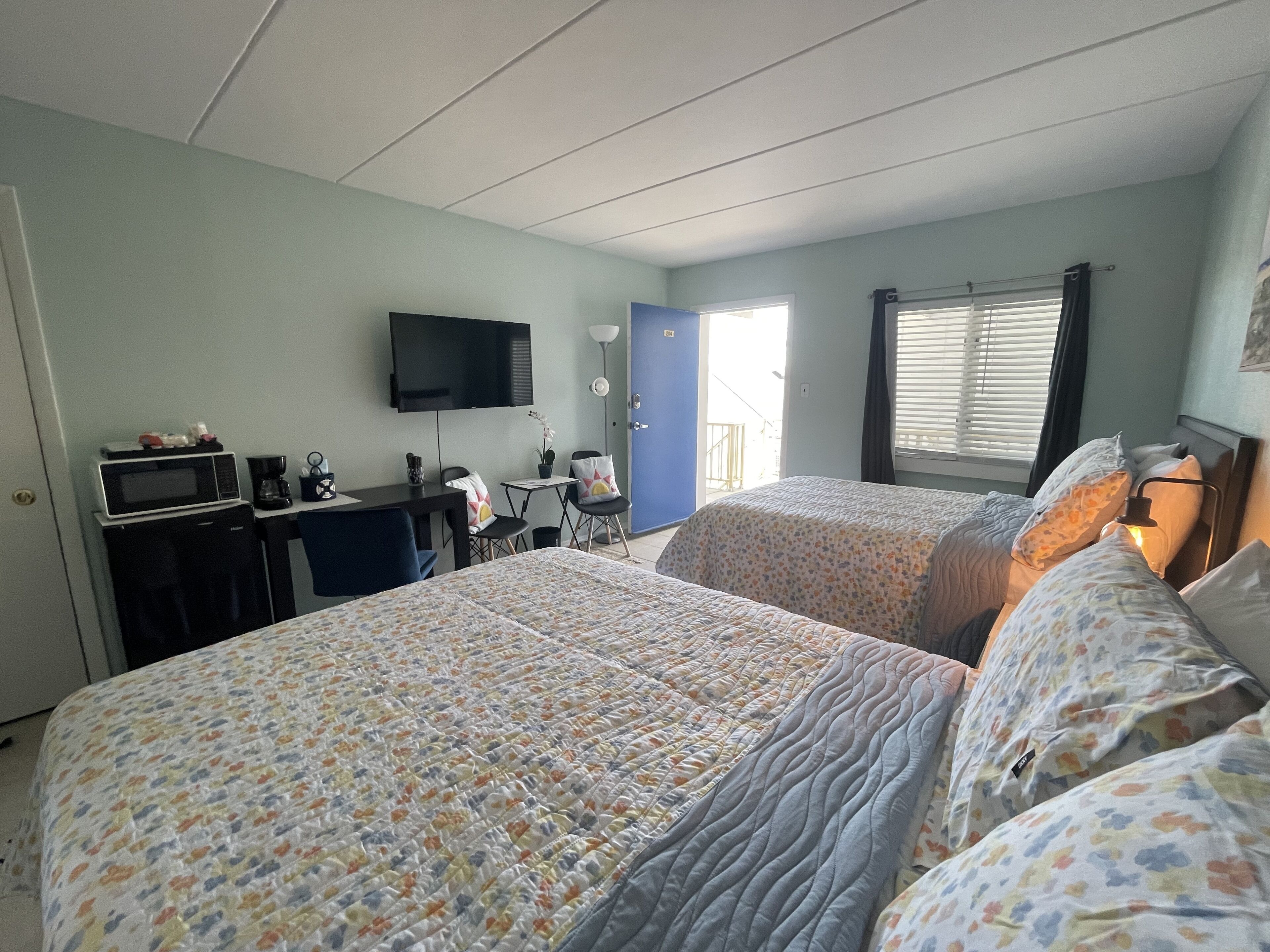 A hotel room with two beds, a desk with a microwave, a TV, and a window with blinds.