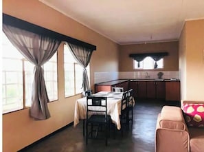 Cozy living space with a dining area and kitchenette, featuring a dining table, sofa, and window with curtains.