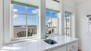 Une cuisine dotée d ’une grande fenêtre, d’un évier et donnant sur un balcon aménagé avec du mobilier d’extérieur.