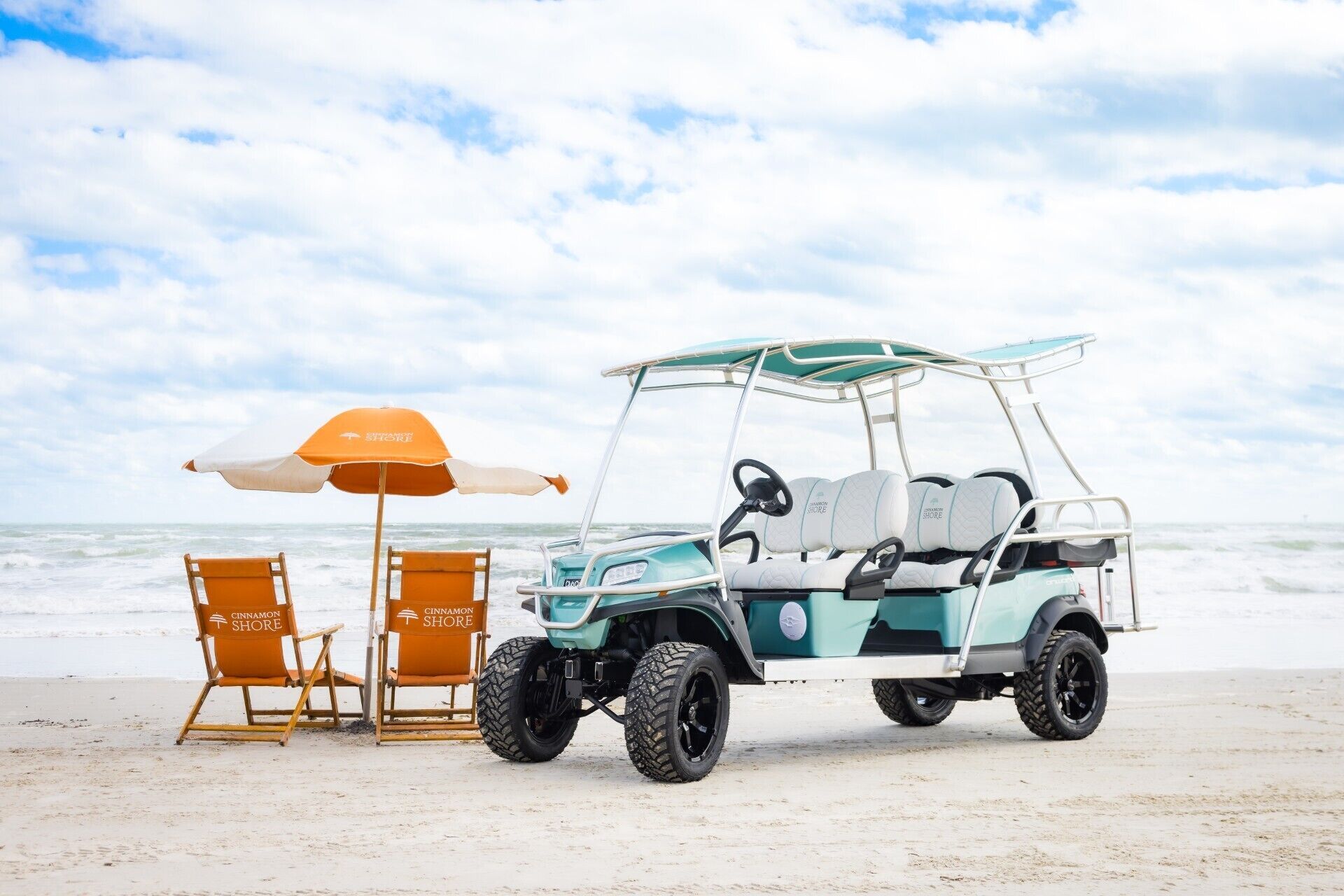 Une scène de plage avec un véhicule de golf, deux chaises de plage et un parasol.