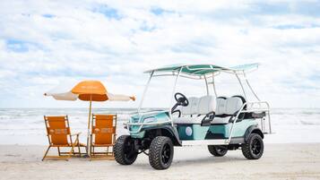 Une scène de plage avec un véhicule de golf, deux chaises de plage et un parasol.