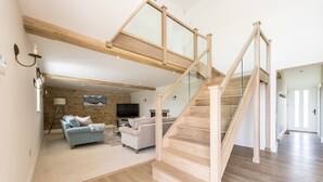 Ein geräumiger Wohnbereich mit einer Holztreppe, einer Steinwand und einem Flachbildfernseher.