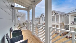 A covered balcony with wicker chairs, white railings, and a view of adjacent buildings. - Pecan Pie 236 BR (Port Aransas)