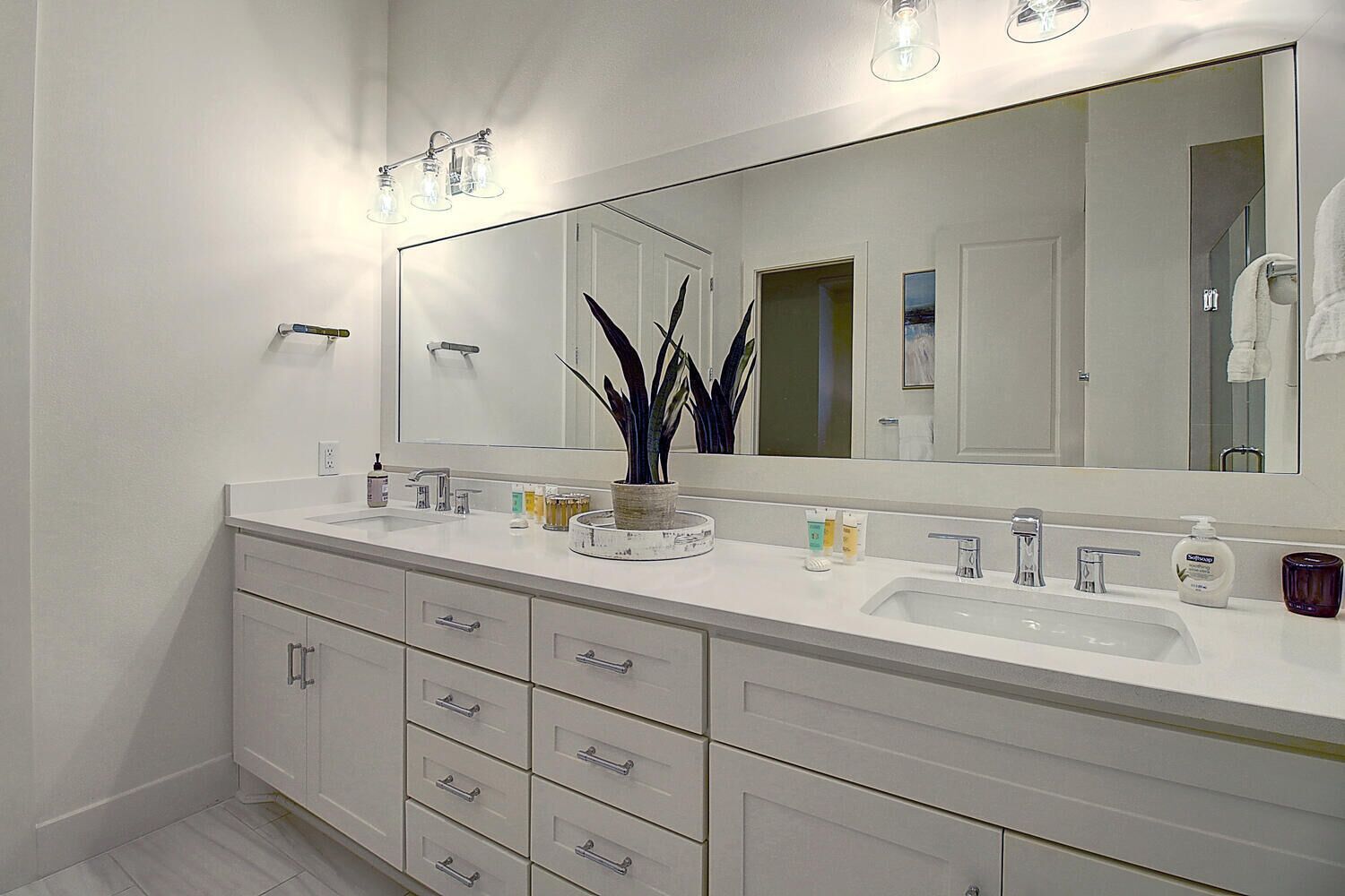A modern bathroom with two sinks, a large mirror, and a potted plant.