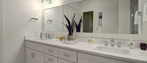 A modern bathroom with two sinks, a large mirror, and a potted plant.