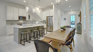 A modern kitchen with white cabinets, a central island with stools, stainless steel appliances, and pendant lighting. - Pecan Pie 236 BR (Port Aransas)