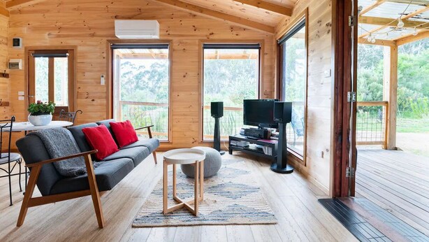 Acogedor interior de cabaña de madera con sofá, televisor y zona de comedor.
