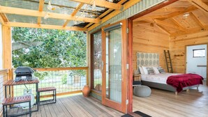 Una cabaña de madera con balcón, cama y parrilla.