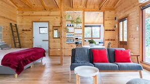 Interior de una cabaña de madera con cama, sofá y zona de comedor.
