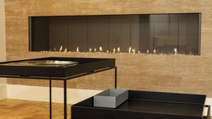 Un interior moderno con chimenea empotrada, una mesa de metal negro y un box gris en un estante bajo.