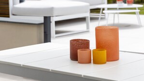 Un espacio al aire libre con mesa y sillas blancas, un sofá blanco con cojines rojos y una pequeña mesa redonda con velas.