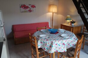 Un comedor con una mesa redonda para cuatro personas, un sofá rojo, una lámpara y un cuadro de flores en la pared.