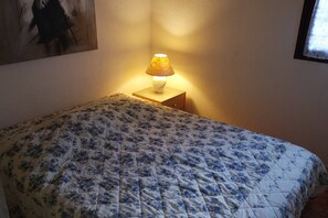 Ein Schlafzimmer mit blumigem Bettbezug, einer Nachttischlampe und einem Bild an der Wand.