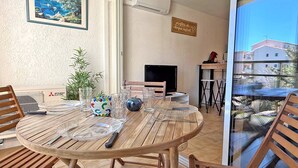 A dining area with a round wooden table, chairs, and a TV. There is a potted plant and a sign on the wall.