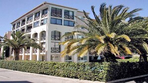 A multi-story hotel with balconies and a well-maintained hedge in front.