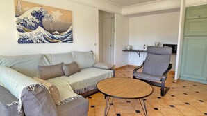 A living room with a sofa, armchair, and coffee table. There is a painting on the wall and a kitchen area in the background. - Apartment for 4/6 people – Swimming pool residence – Air conditioning – WiFi – Sainte Maxime (STE MAXIME)