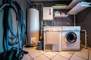 Uma lavanderia com máquina de lavar, secadora, aquecedor de água e aspirador de pó.