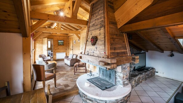 A spacious living room with a stone fireplace, wooden beams, and a view of the adjacent room. - 14 person chalet, 100m from the Super-Chatel gondola - Chatel Reservation (Châtel)