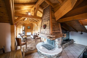 Un salón espacioso con chimenea de piedra, vigas de madera y vista al salón contiguo.