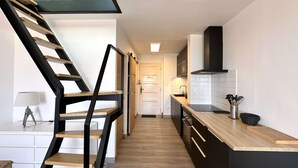 Eine moderne Küche mit einer Holztreppe, einer Kücheninsel und Blick in den Flur.