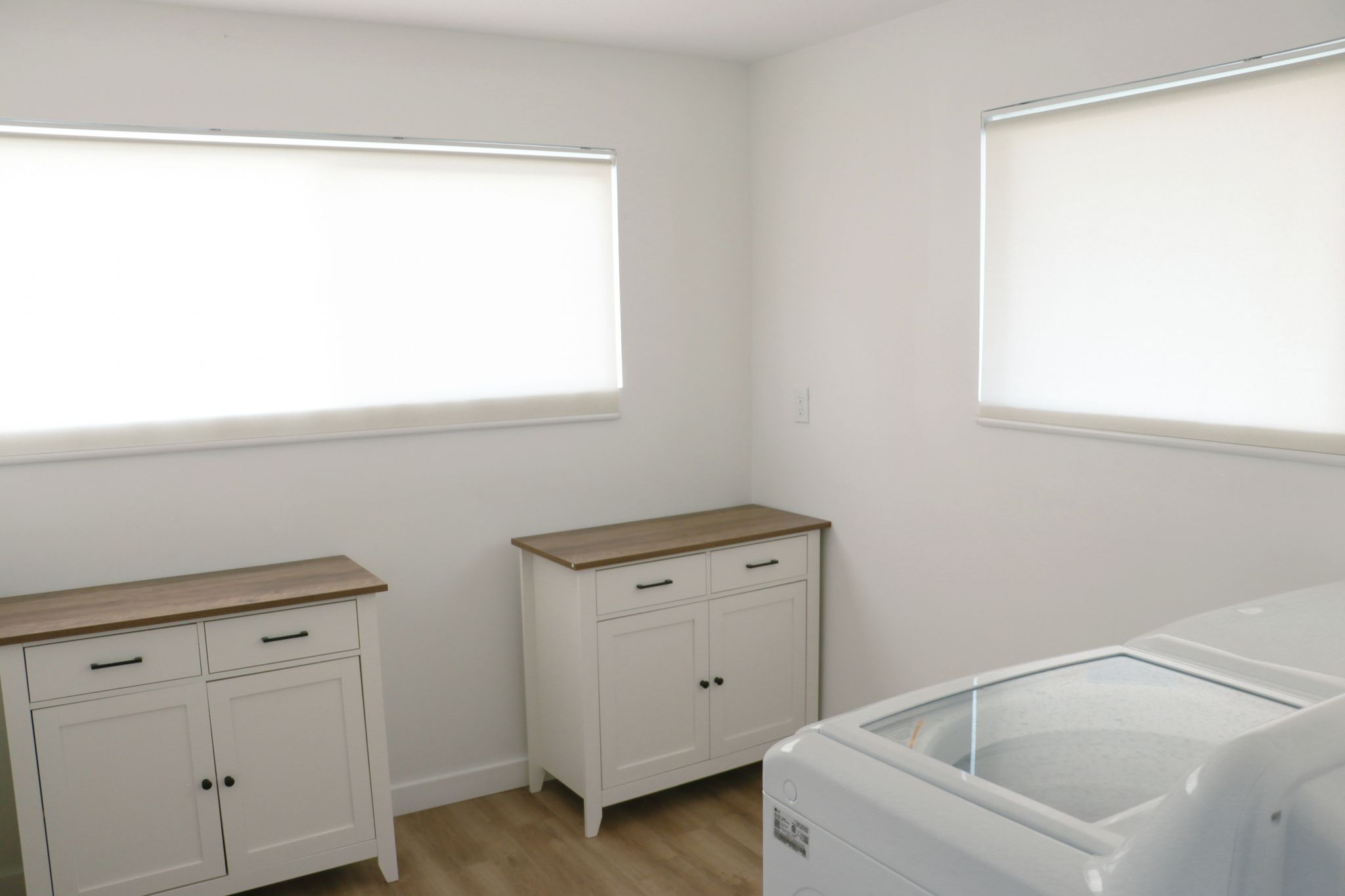 Een kamer met een witte kast, een klein meubelstuk en een wasmachine.