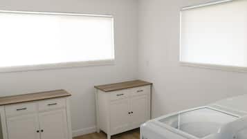 Een kamer met een witte kast, een klein meubelstuk en een wasmachine.