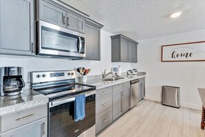 A modern kitchen with stainless steel appliances, grey cabinets, and a coffee maker.