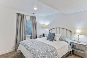 A bedroom with a bed, two bedside tables, a lamp on each table, and a window with curtains. - Spacious Home for Amazing long term stays! (Vineyard)