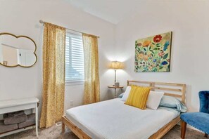 A bedroom with a bed, a bedside table, a lamp, a chair, a mirror, and a floral painting on the wall. - Spacious Home for Amazing long term stays! (Vineyard)